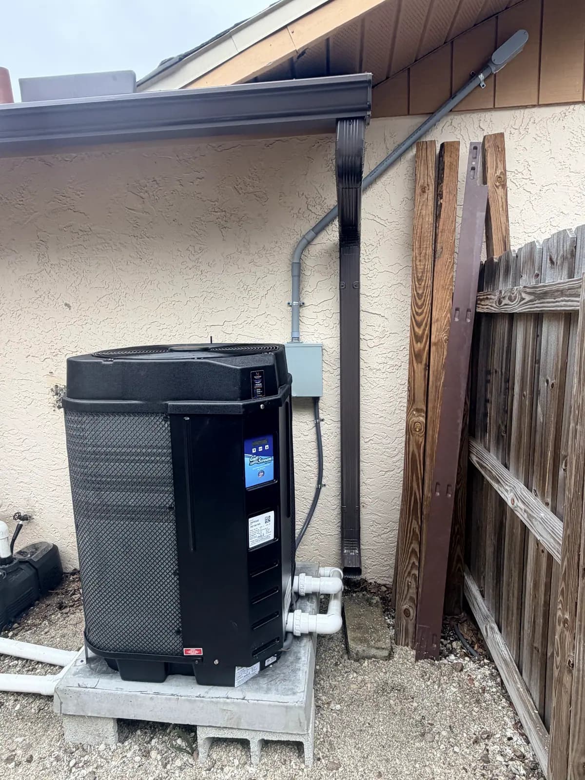 GulfStream HE150-RA heat pump on a raised concrete base in a gravel side yard beside a wood fence