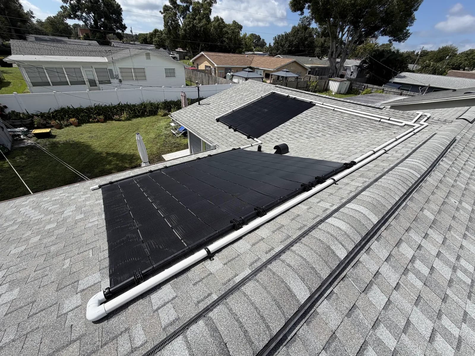 Solar pool heating collectors on a gray shingle roof with white PVC supply and return lines